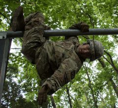 A Cadet hangs from a raised bar on an FLRC obstacle.