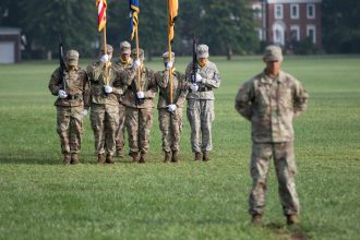 Five Five Cadets hold flags at the graduation ceremony while another Cadet stands in front of them. 