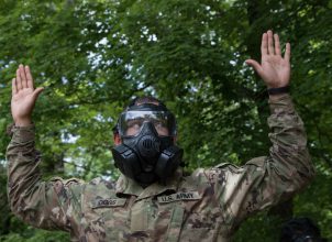 A Cadet raises his arms while wearing a gas mask.