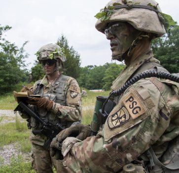 A West Point Cadet stands next to a ROTC Cadet while writing in a notebook.