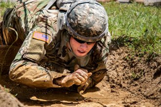 A Cadet crawls through the mud to the next obstacle